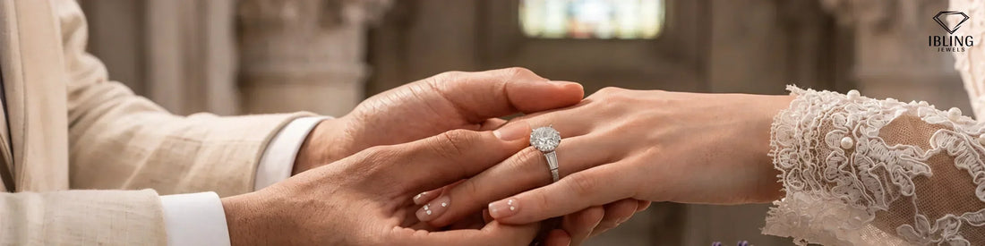 Close up view of a groom placing a round diamond white gold engagement ring with baguette side stones on a bride's finger.