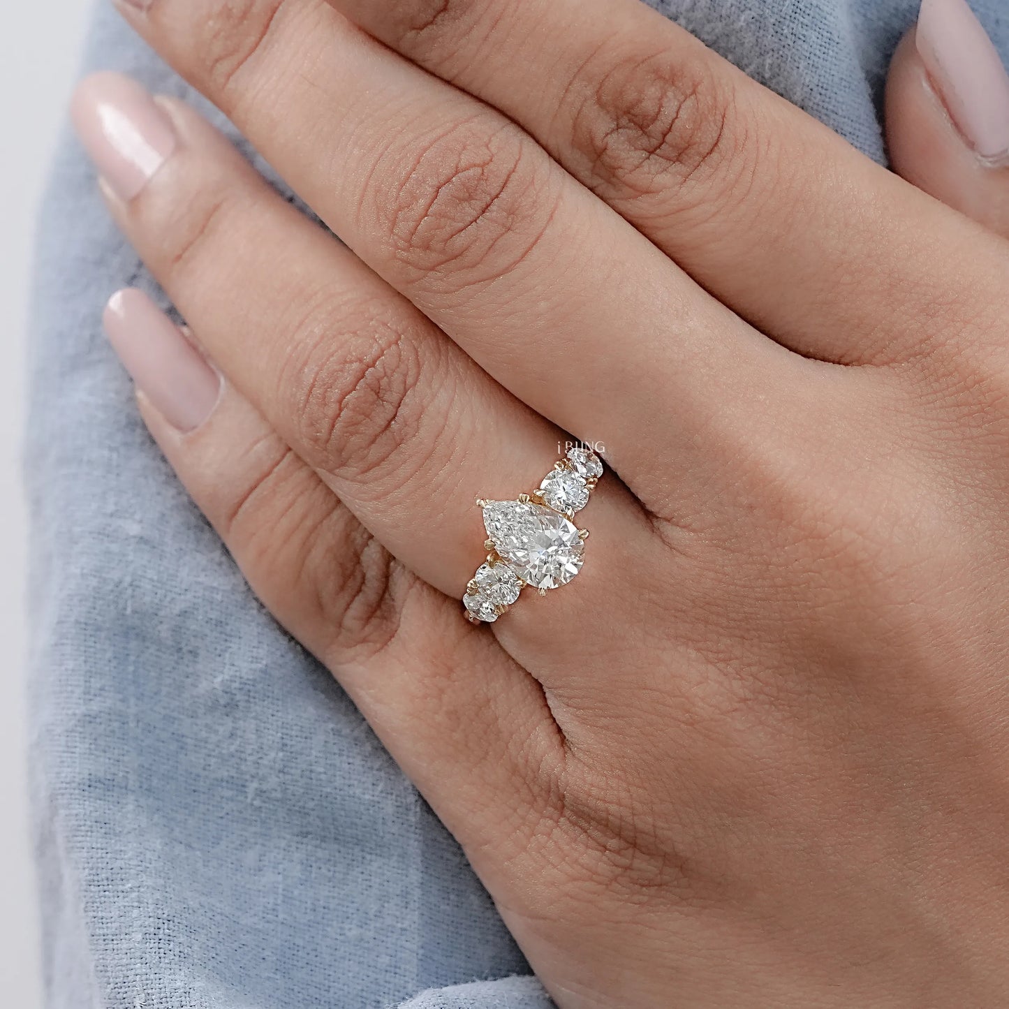 Woman Hand Wearing Five Stone Pear and Round Cut Synthetic Diamond Engagement Ring