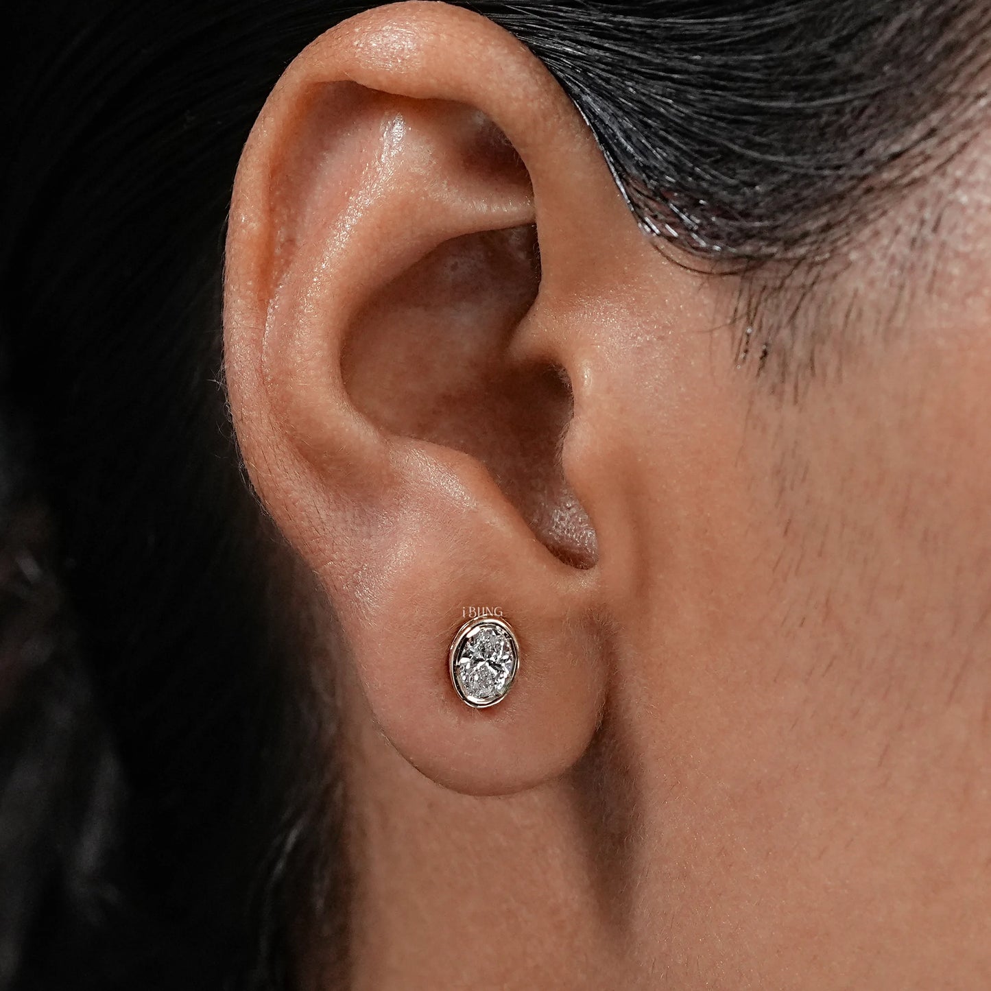 Woman hand holding Oval Bezel Set Lab Grown Diamond Stud Earrings, ideal anniversary or bridal gift