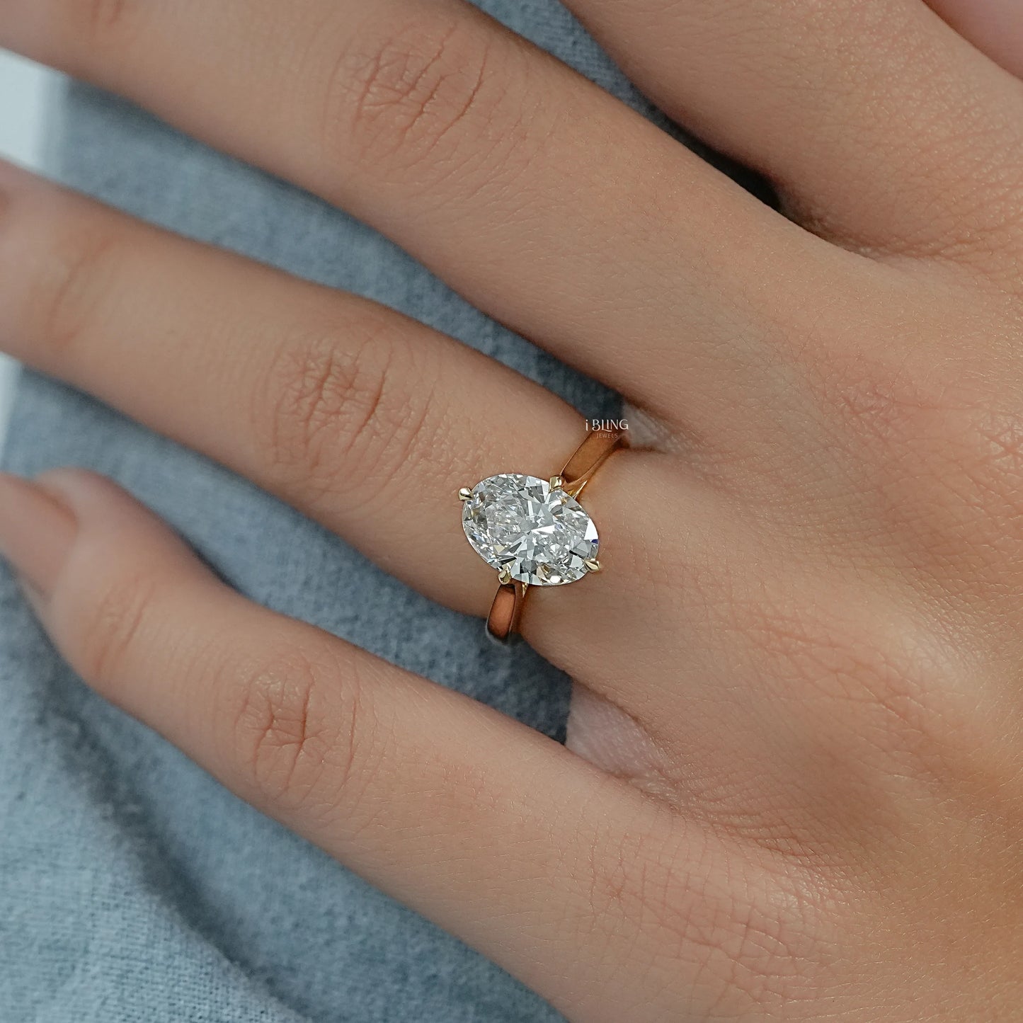 Hand wearing a 2 carat diamond oval ring in yellow gold with a refined and slender silhouette.